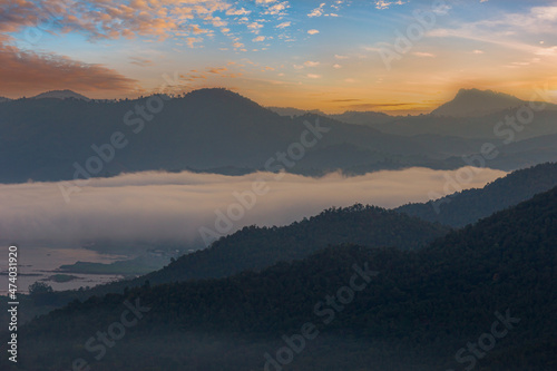 Mountains in clouds at sunrise in summer. Aerial view of mountain peak in fog. Beautiful landscape with high rocks, forest, sky.