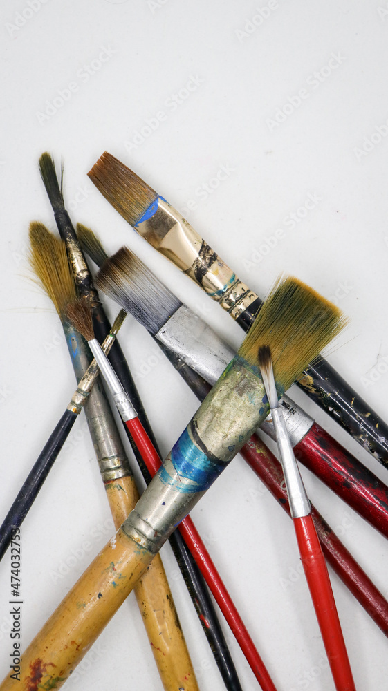 Obraz premium vertical shot of a group of wooden and plastic artists paint brushes different shapes and sizes, with color stains laying on each other isolated in a white background
