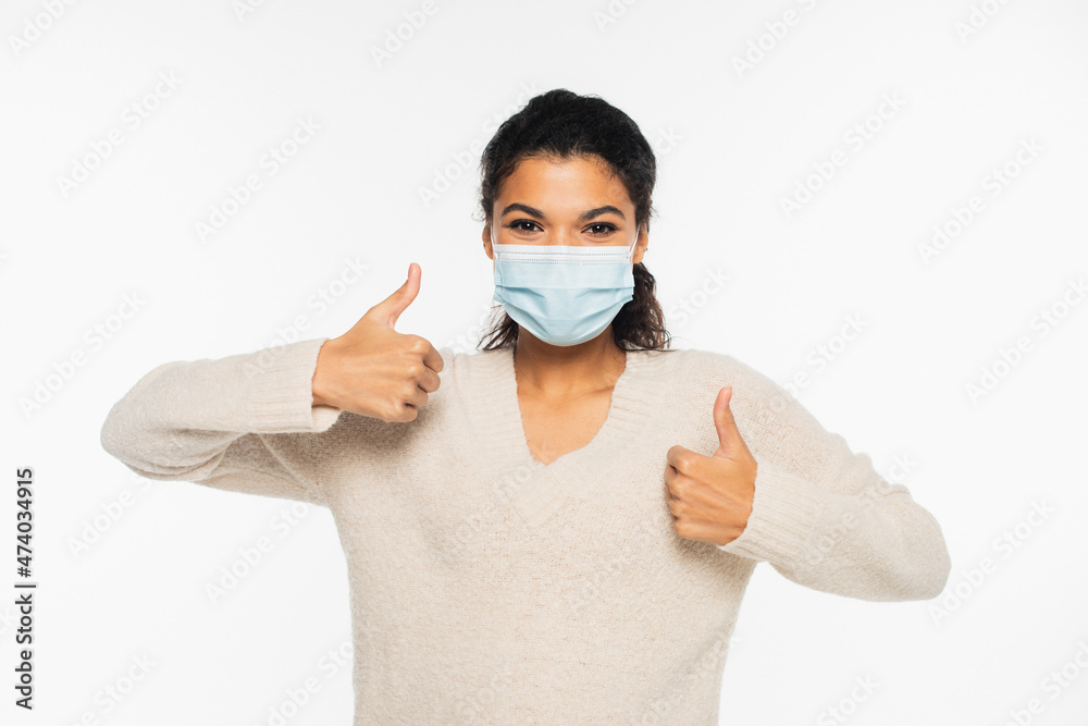 Young african american woman in medical mask showing like gesture isolated on white. Young african american woman in medical mask showing like gesture isolated on white.