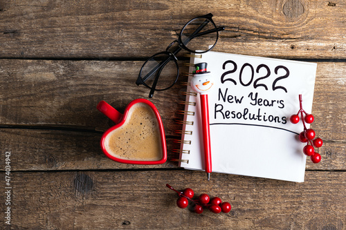 New year resolutions 2022 on desk. 2022 new year resolutions on wooden background with coffee cup, notebook and christmas decorations. New year goals, plan, resolutions, business concept