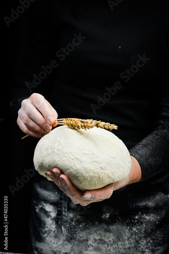 Female hands holding a piece of dough for baking bread. Black cooking background.