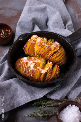 Hasselback potato roasted with cheese, bacon and aromatic herbs served in cast iron skillet. Hot meal photo