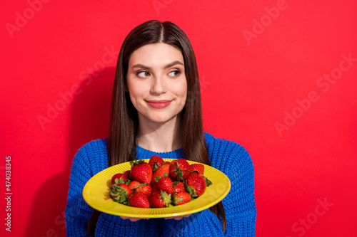Photo of lovely young woman look empty space hold hands plate strawberry isolated on red color background