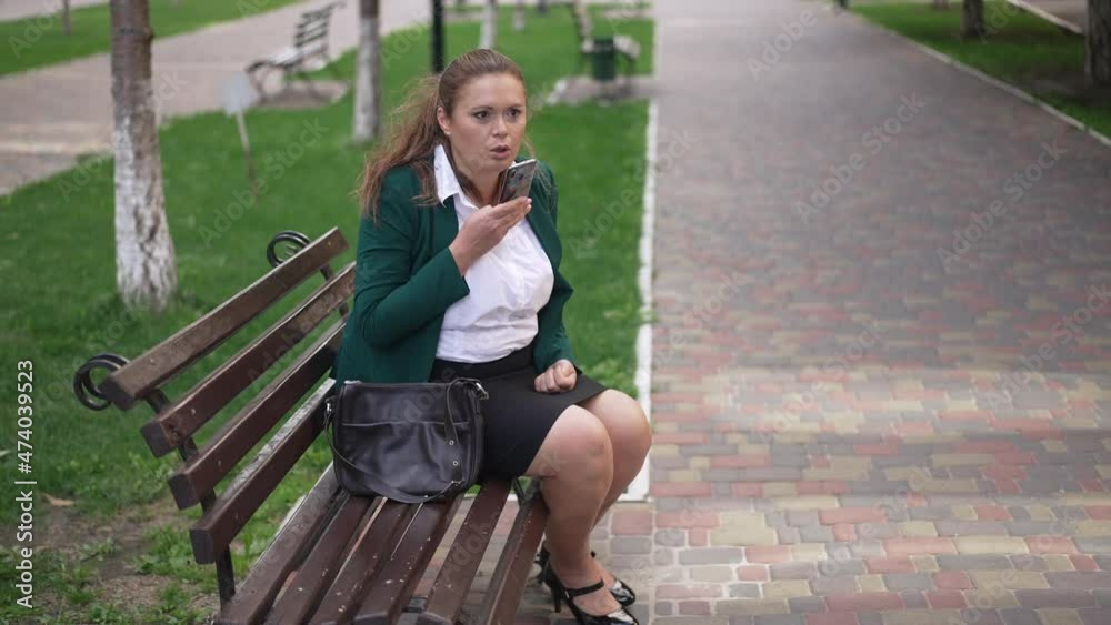 Wide shot portrait serious confident female plus-size CEO sitting on bench in city recording voice mail. Successful beautiful overweight Caucasian businesswoman managing business outdoors Wide shot portrait serious confident female plus-size CEO sitting on bench in city recording voice mail. Successful beautiful overweight Caucasian businesswoman managing business outdoors