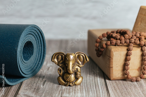 Close-up bronze statue of hindu god of success Ganesha. Japa Meditation accessories, mat and yoga wooden blocks on wooden background.