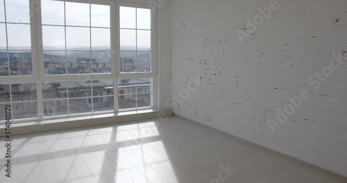 A door is opening and the camera enters an empty unfurnished room interior with a wooden parquet floor, white walls, and big windows. 4k slow motion