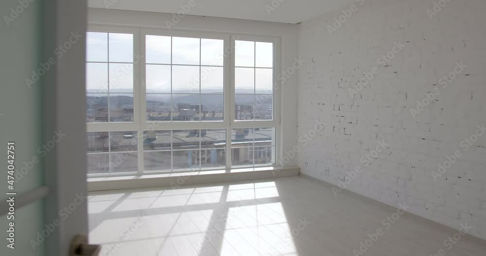 A door is opening and the camera enters an empty unfurnished room interior with a wooden parquet floor, white walls, and big windows. 4k slow motion