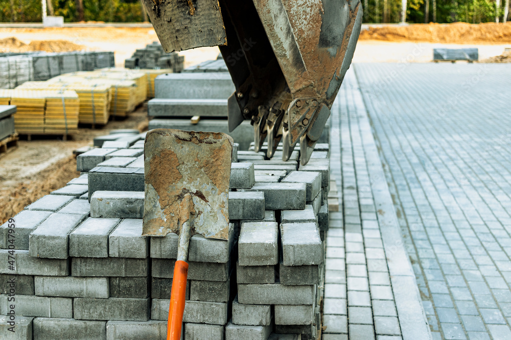 A mini excavator bucket rests on a pallet of paving slabs at a construction site. Compact construction equipment for earthworks and landscaping.