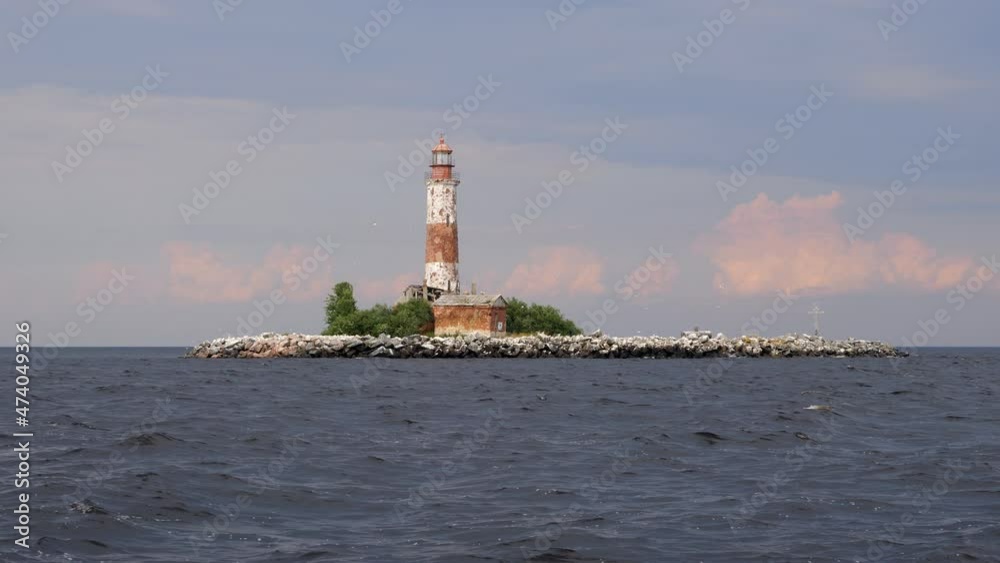 Nice small artificial island with old lighthouse in beautiful pastel colors. Dark water of lake, pink cumulus and high blue clouds on background. Picturesque shot of Sukho island at Ladoga Lake Nice small artificial island with old lighthouse in beautiful pastel colors. Dark water of lake, pink cumulus and high blue clouds on background. Picturesque shot of Sukho island at Ladoga Lake