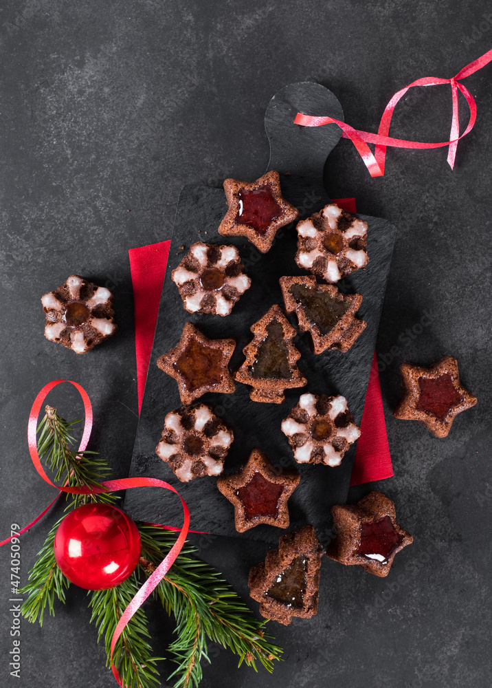 Christmas chocolate cakes cookies in the shape of a tree, snowflakes, stars with marmalade on a serving board on a dark background. Top view 