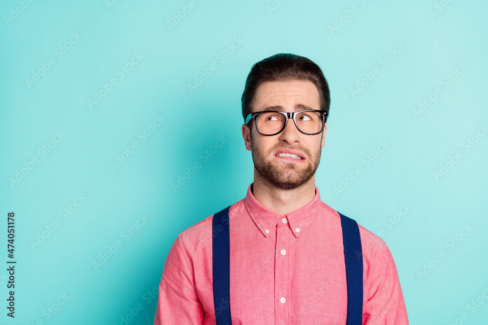 Fototapeta premium Photo of doubtful unhappy upset young man look empty space wear glasses bite teeth isolated on teal color background