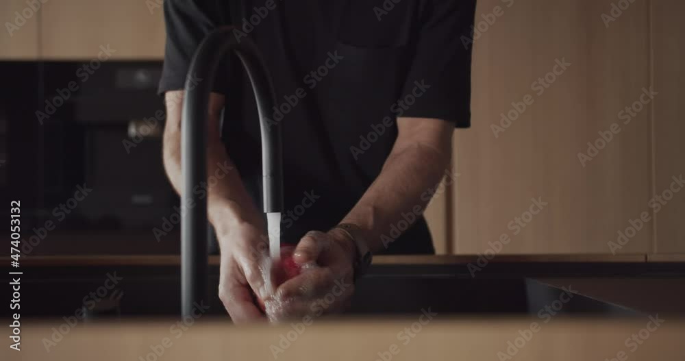 A man washes a grapefruit in a modern kitchen with a minimalist interior