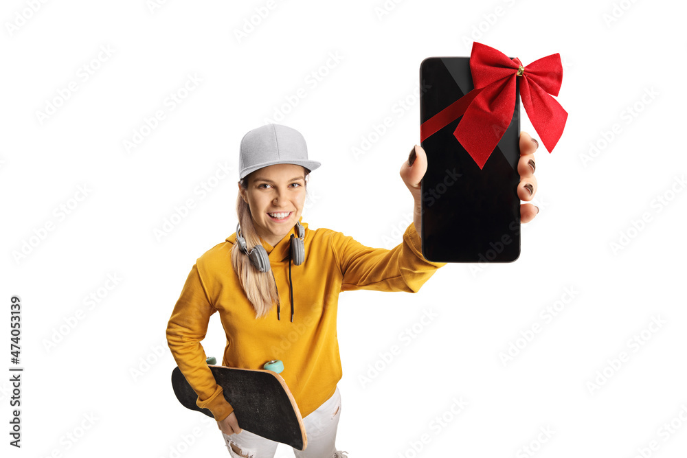 Female teen with headphones and a skateboard holding a smartphone with red bow in front of camera Female teen with headphones and a skateboard holding a smartphone with red bow in front of camera