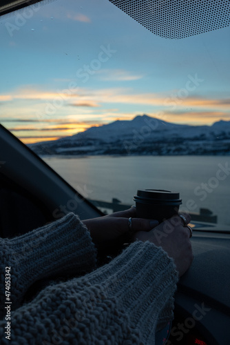 woman watching the sunset in cozy car with mountain landscape and coffee