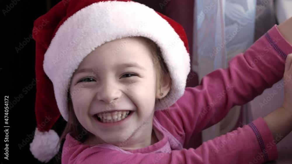 A little girl 3 years old in a Santa hat looks into the frame with big beautiful blue eyes. Close-up portrait of a christmas child. She smiled and said congratulations. A little girl 3 years old in a Santa hat looks into the frame with big beautiful blue eyes. Close-up portrait of a christmas child. She smiled and said congratulations.