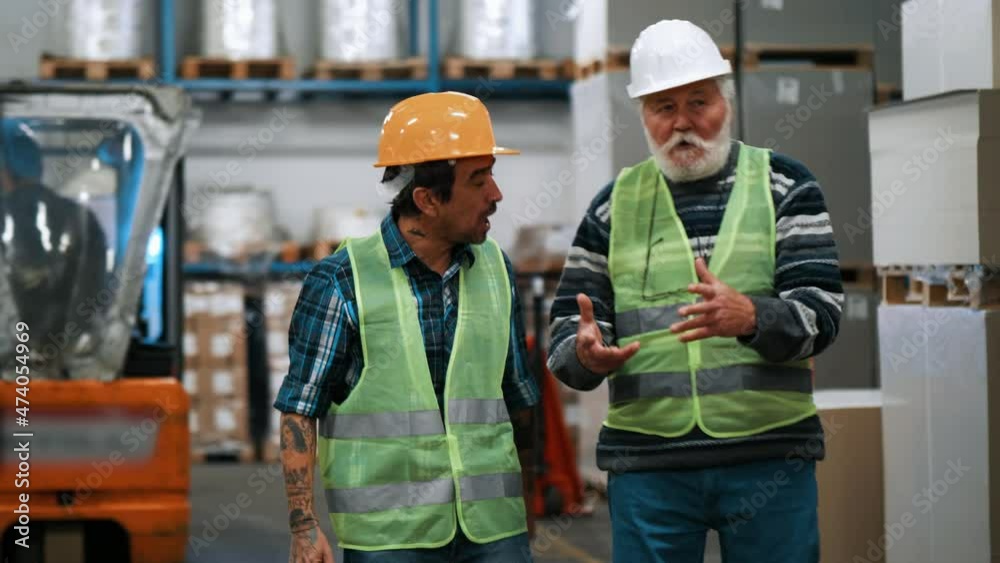 Two workers engineers talking in the factory walking through rows of storage Two workers engineers talking in the factory walking through rows of storage