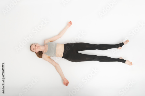 Shavasana. Corpse Pose. Yoga asanas. Young slender woman in sportswear lies on the white floor . Top view.