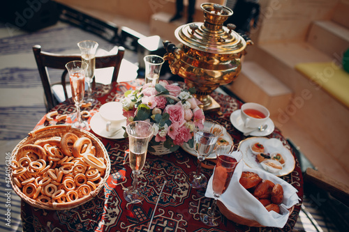 Old traditional Russian table for tea drinking with samovar, glasses of wine, flowers, pastries, bagels and buns