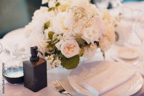 round tables in the restaurant with white tablecloths and white bouquets of flowers decor with hand sanitizer.