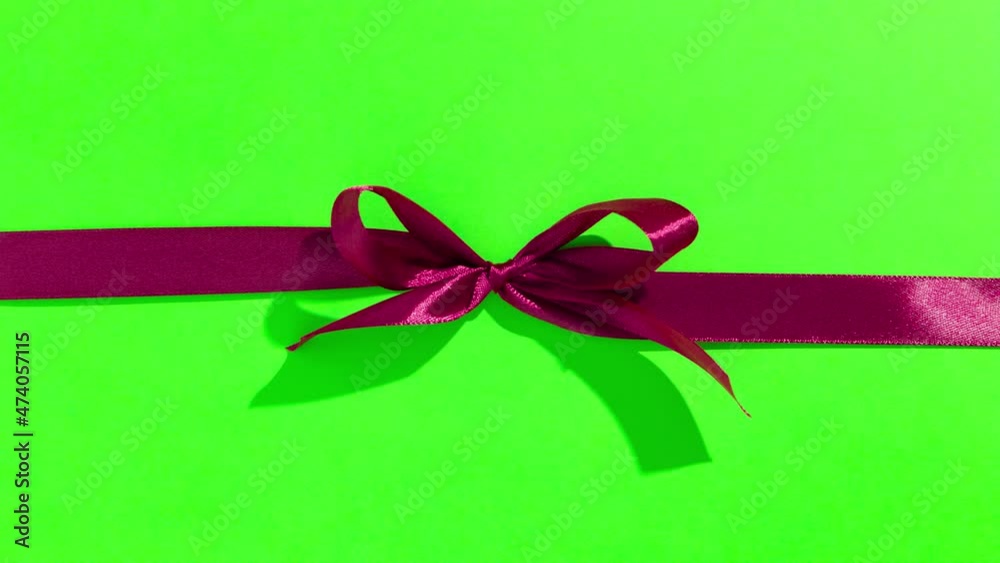Red ribbon with bow on green screen, opening and unpacking a gift, top view - Stop motion animation for Valentine's Day, Christmas.