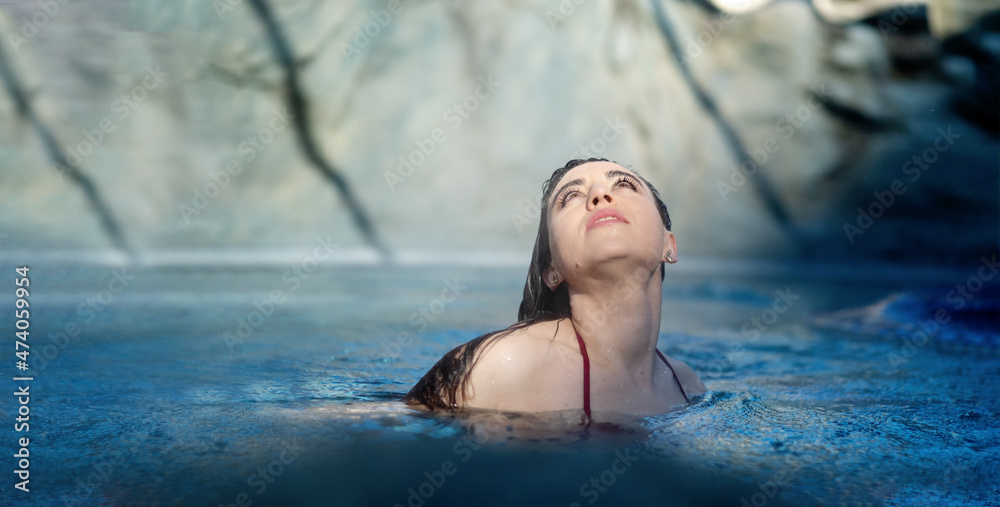 Portrait of beautiful mature woman with dark hair relaxes contend happy in holidays summer sun in the blue spa wellness whirlpool, raised eyes, looking up to the sunny sky