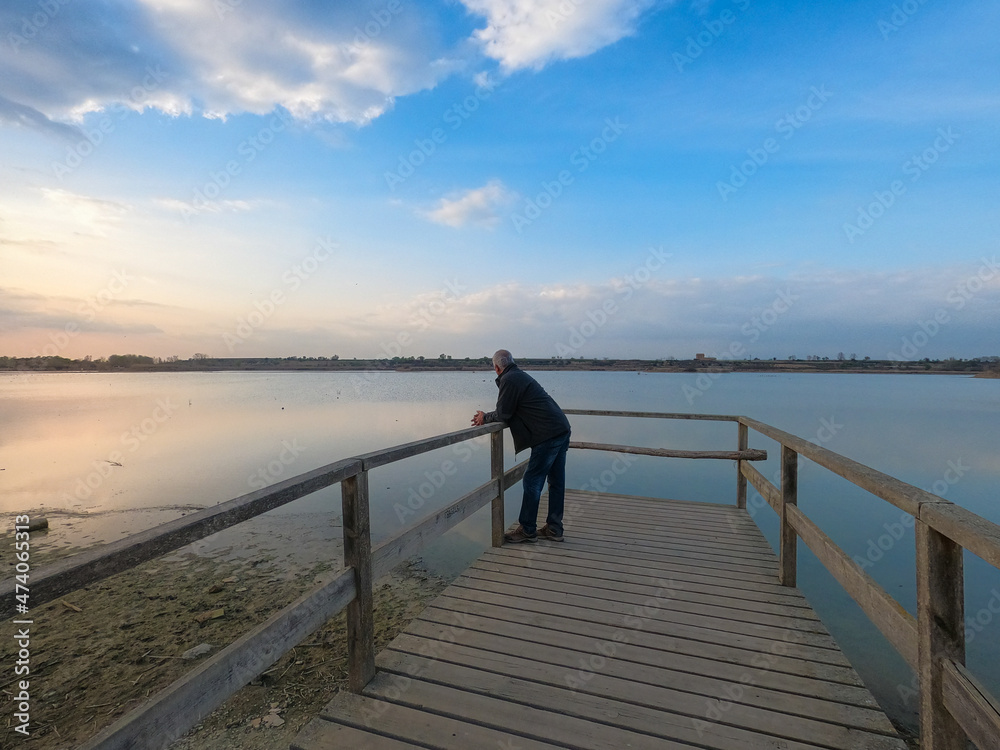 Older man watching the sunset on the lake pier on a winter day.