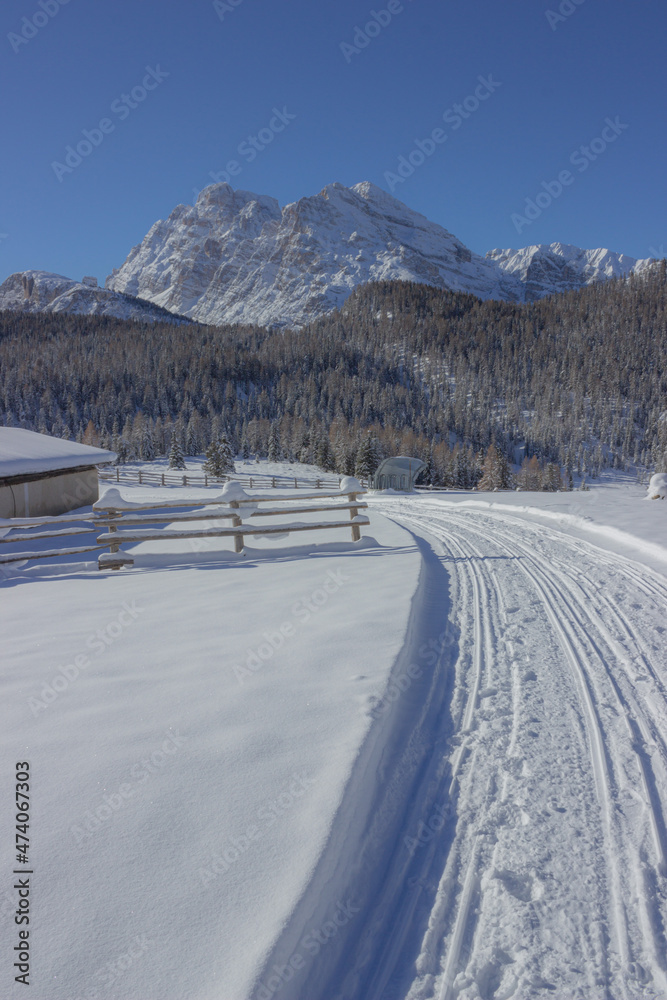 View on the beautiful winter mountain road. Snowmobile beaten road that runs near a fence towards the mountain. View from the road to Tre Cime di Lavaredo. Vertical image.