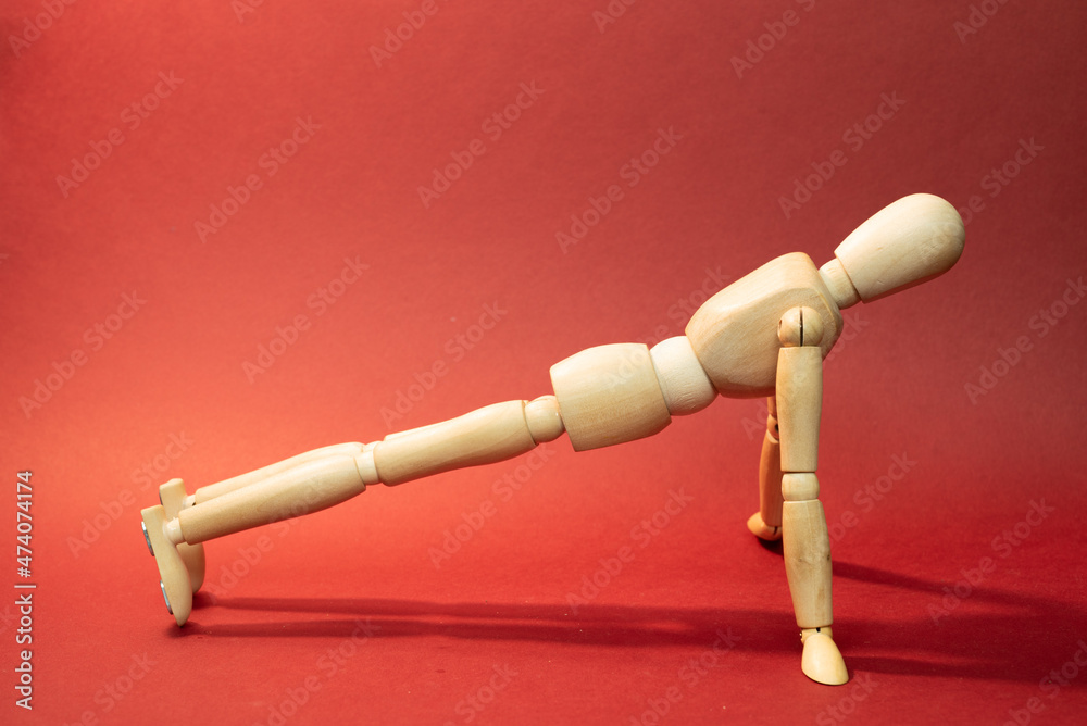 Wooden mannequin staying in plank Pose, Intense Stretch Pose, doing sport exercises , push-ups , picture on red background Wooden mannequin staying in plank Pose, Intense Stretch Pose, doing sport exercises , push-ups , picture on red background
