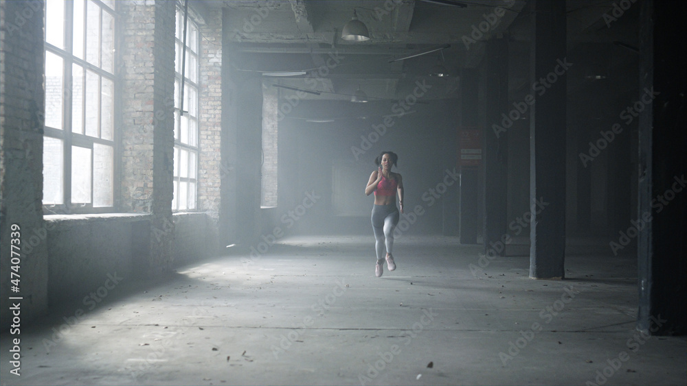 Sportswoman training in loft building. Female jogger running in gym Sportswoman training in loft building. Female jogger running in gym