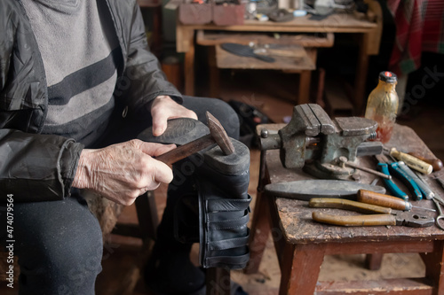 A retired shoemaker repairs shoes. There are many instruments near it.