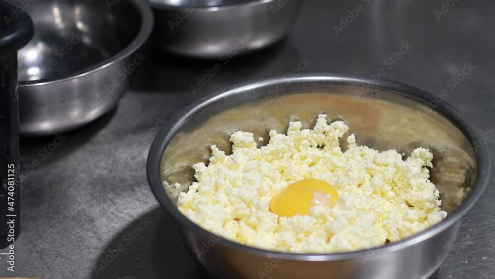 the cook stirs the egg yolk in a bowl with cottage cheese, metal dishes, dessert preparation the cook stirs the egg yolk in a bowl with cottage cheese, metal dishes, dessert preparation