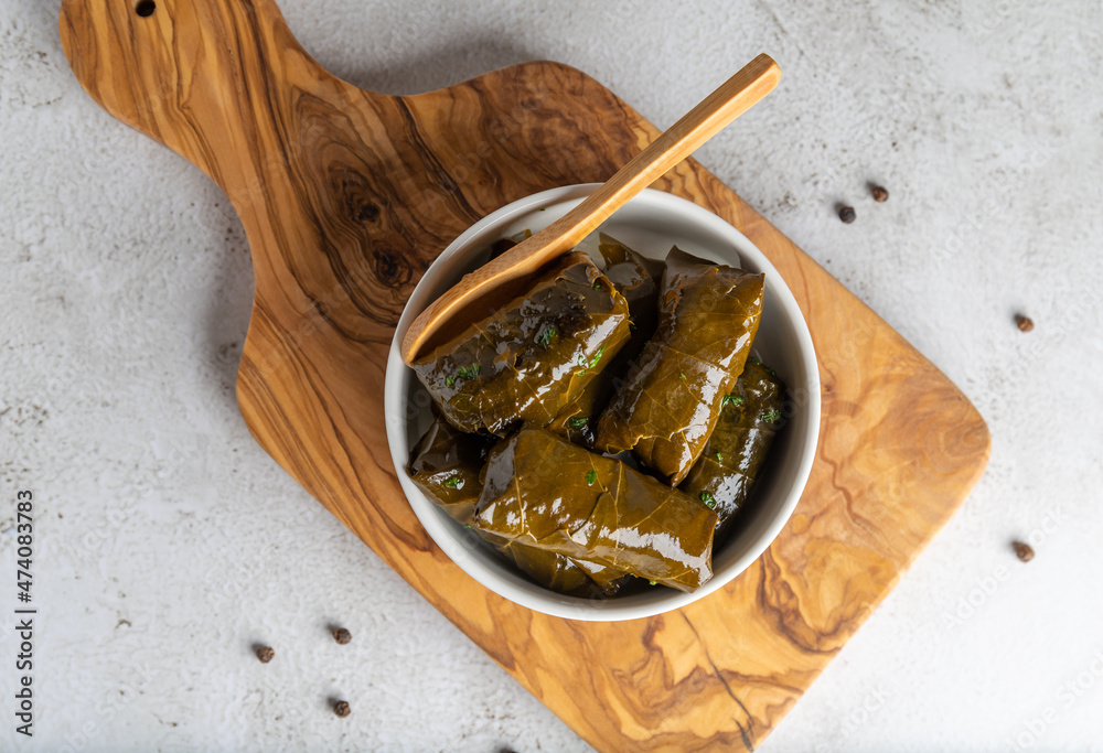Stuffed grape leaves in olive oil in a bowl on the olive wood cutting board, photographed from above Stuffed grape leaves in olive oil in a bowl on the olive wood cutting board, photographed from above