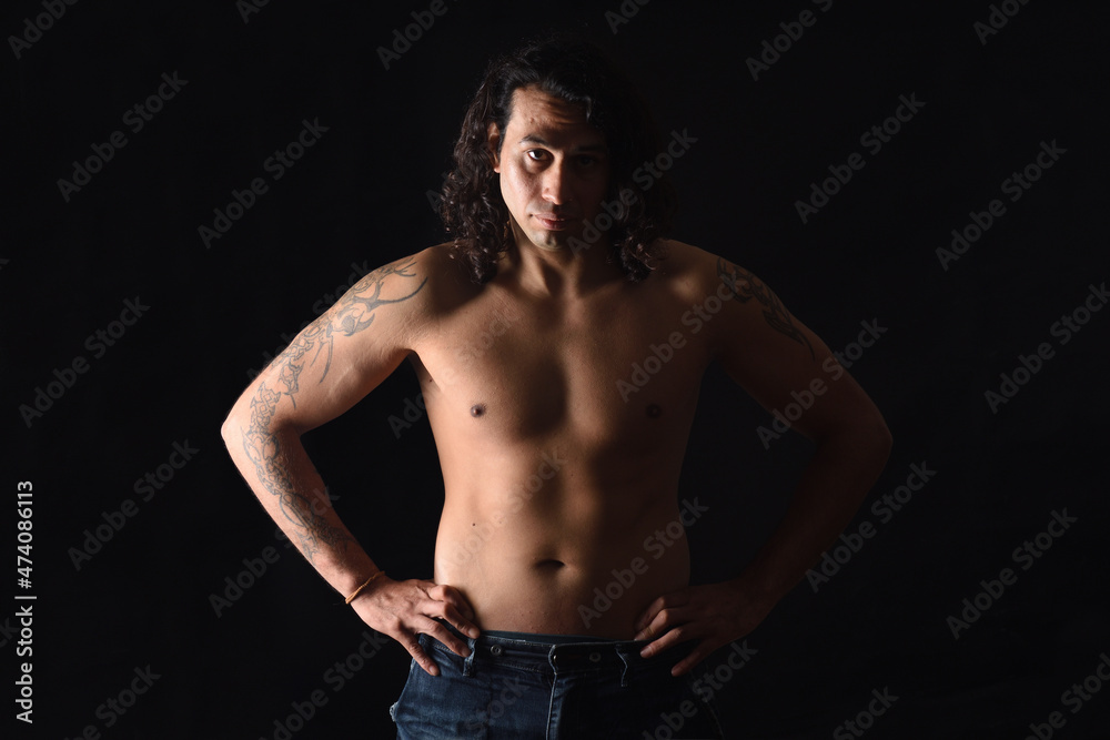 low key portrait of a man with tattoo looking at camera and hands on waist on black background low key portrait of a man with tattoo looking at camera and hands on waist on black background