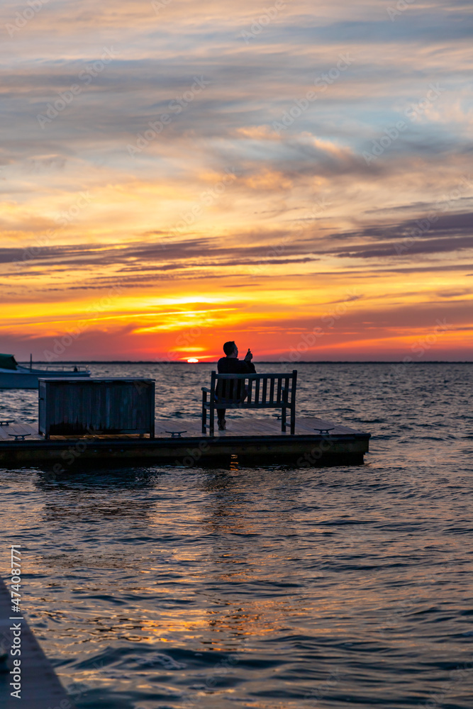 Man sitting on dock taking photos of incredible sunset.
