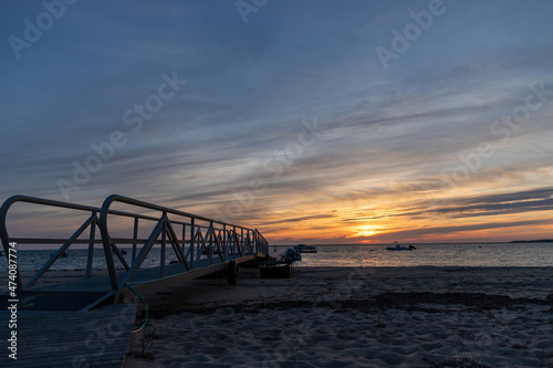 Beach dock leading out to the ocean during sunset. © Cavan