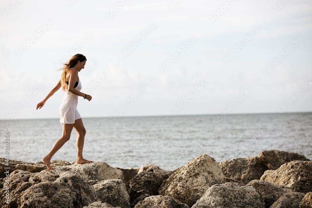 An attractive woman walks barefoot across jetty at the water edge An attractive woman walks barefoot across jetty at the water edge