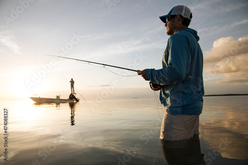 A fisherman wades while fly fishing in keys with boat in background