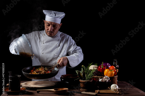 Male chef in white uniform pouring boiled spaghetti into pan wok for cooking pasta with vegetables.