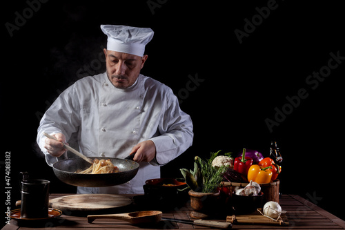Male chef in white uniform preparing spaghetti into cooking pan for cooking pasta with vegetables.