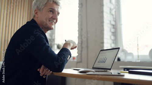 A man of stylish age gray-haired workplace in the office. Works smiling on the internet on an online site. © muse studio