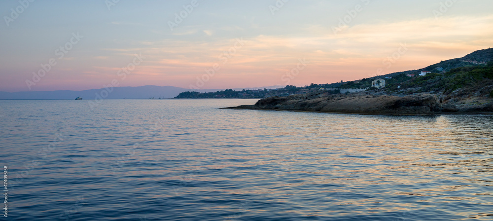 Calm nature scenery landscape of sea at sunset time with rocky seashore and a boat on horison