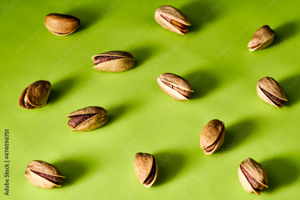 peeled pistachios on green background, top view