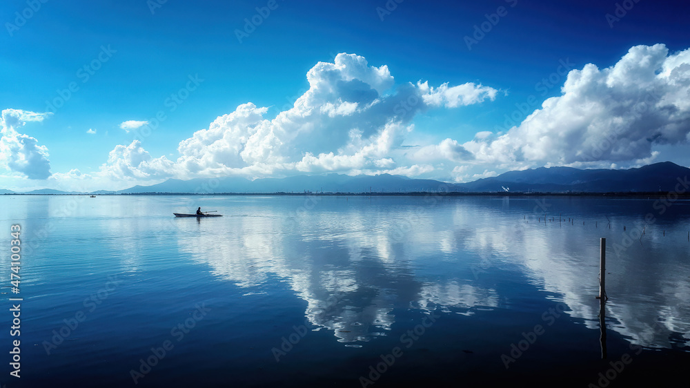Stunning panorama of a sky with white clouds reflected on the calm sea water. Small fishing boat that sails on the flat sea with a spectacular sky, large white cumulonimbus clouds. Sea mirror effect.