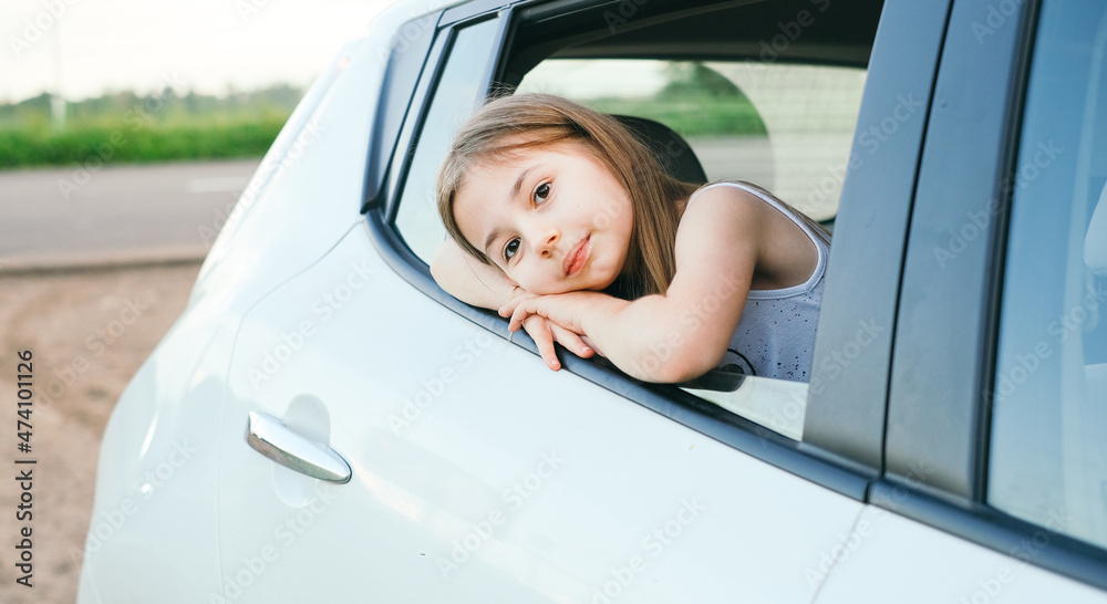 A little girl is sticking her head out the car window and looking down for a road trip or travel concept