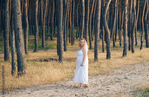 plus size girl in a pine forest at sunset in a white femine sundress