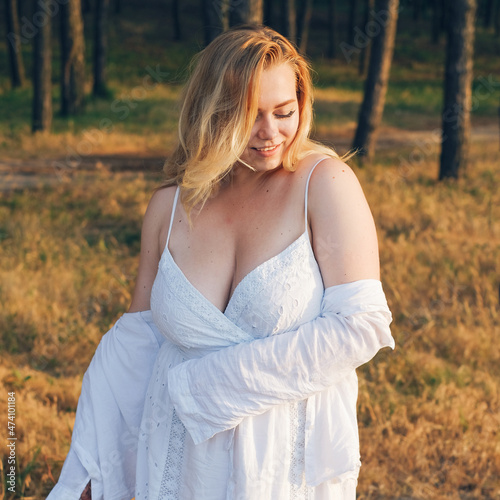 plus size girl in a pine forest at sunset in a white femine sundress