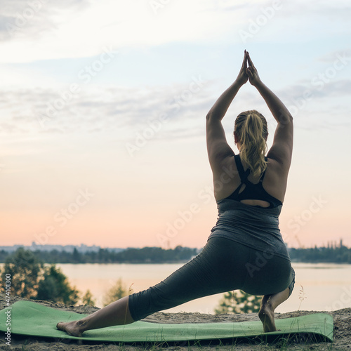 Morning yoga. Young woman plussize doing exercises near the lake,back view. Healthy lifestyle, sport, weight losing, activity concept