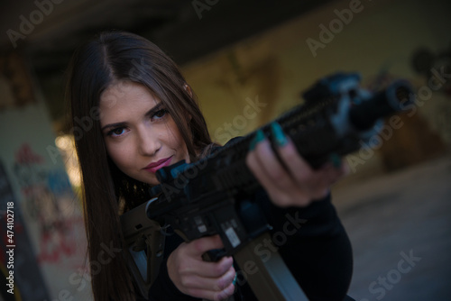 Girl with an air soft rifle in a black tight long-sleeved T-shirt and camouflage cargo pants © Dusan