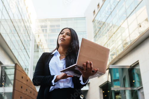 Elegant businesswoman working standing with her laptop in an office building in the financial center of a city. photo