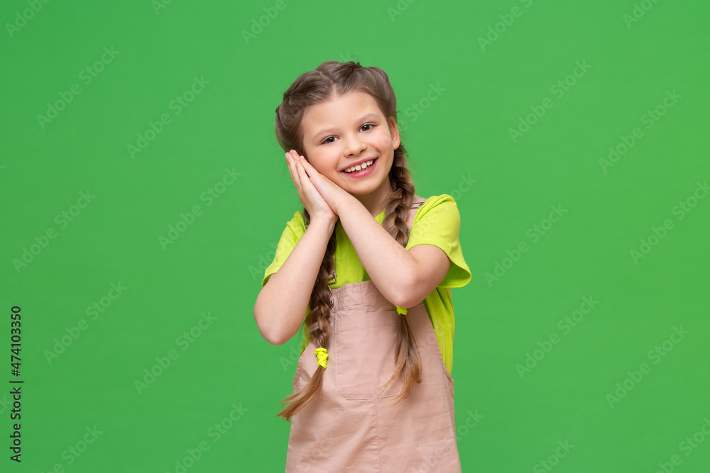 The little girl put her hands to her cheek and looks forward smiling.